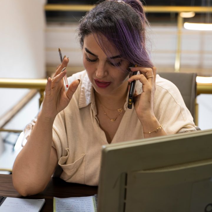 Ongoing Support Woman talking on the phone while holding a pen and looking at paperwork.