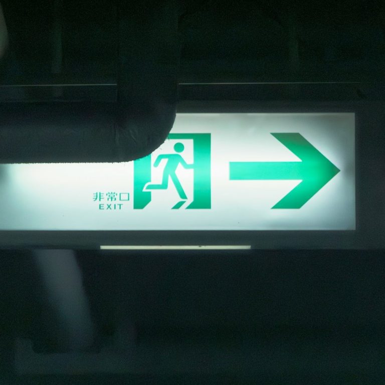 Comprehensive Audits Green exit sign with an arrow pointing right and a figure running.