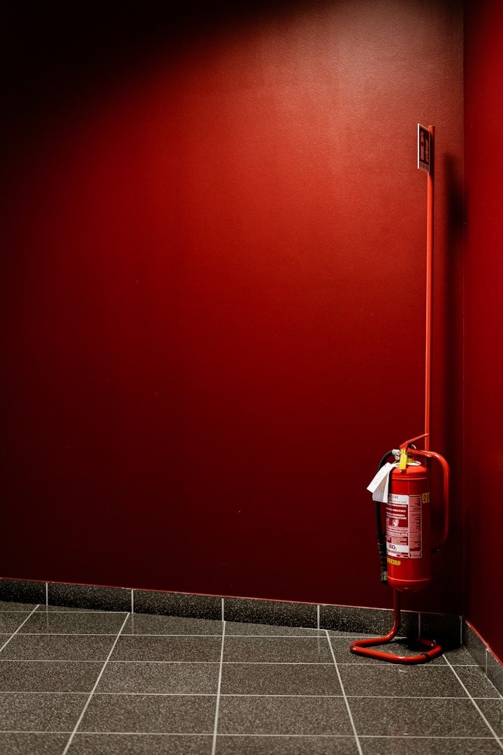 Fire Extinguisher Red fire extinguisher mounted on a wall in a dimly lit corner with dark tiles.